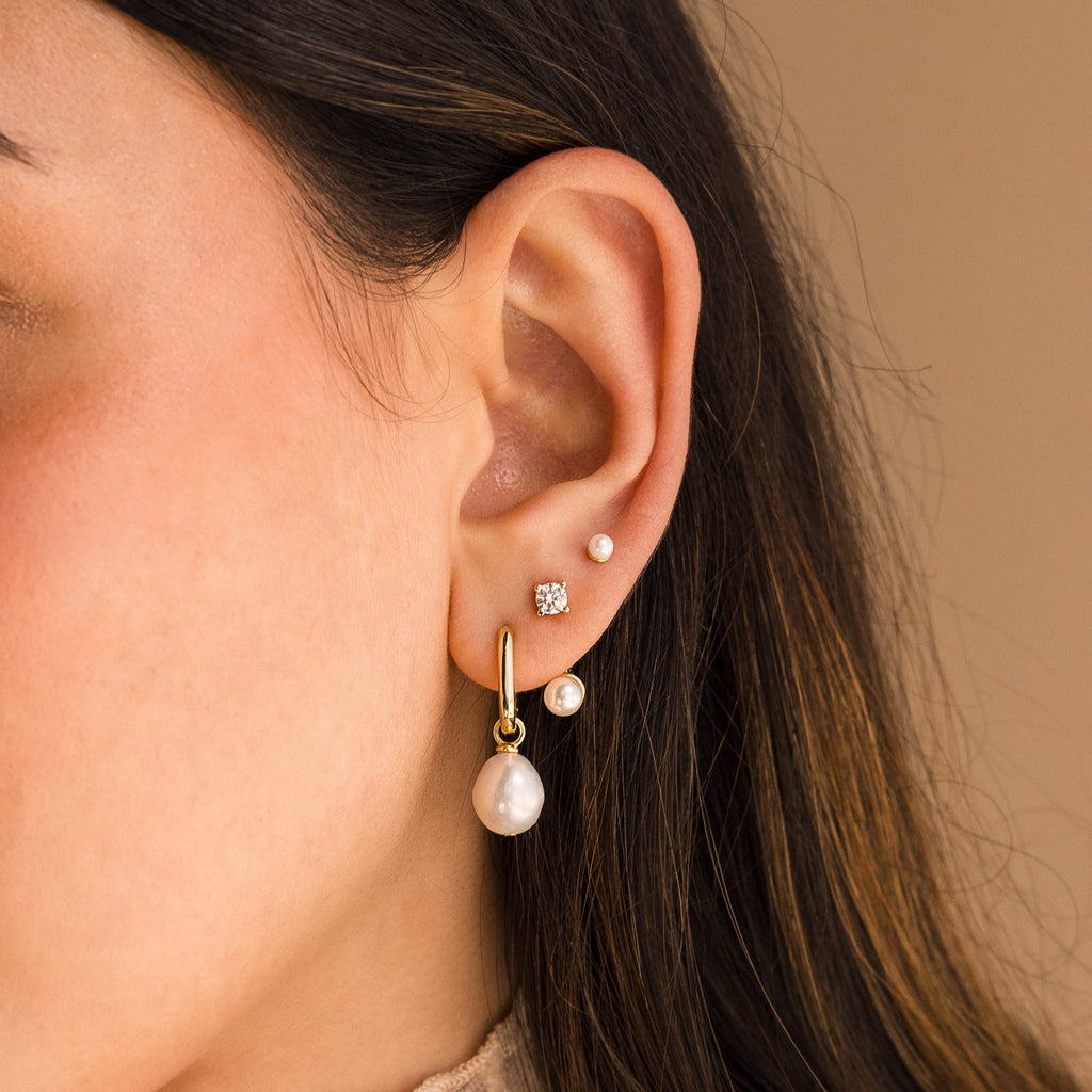 Close-up of an ear with four piercings adorned with elegant jewelry, including Freshwater Pearl Drop Hoops alongside gold hoops and diamond studs.