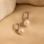 Freshwater Pearl Drop Hoops with elegant pearl drops are shown on a beige fabric background with stone accents, highlighting timeless style.