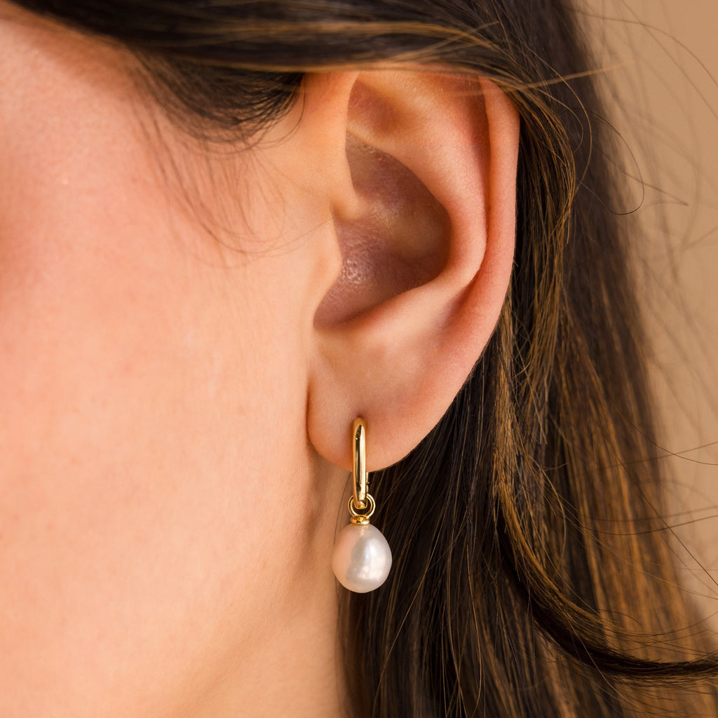 Close-up of a woman's ear wearing Freshwater Pearl Drop Hoops, featuring a gold hoop with a dangling white freshwater pearl for an elegant look.