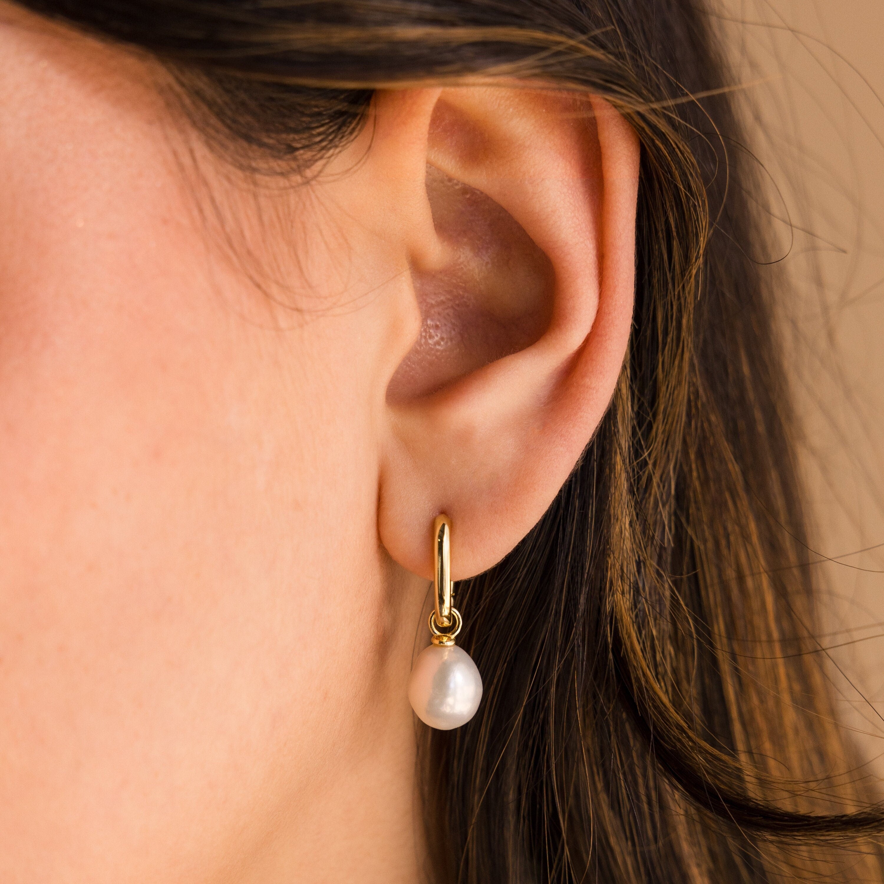 Close-up of a woman's ear wearing Freshwater Pearl Drop Hoops, featuring a gold hoop with a dangling white freshwater pearl for an elegant look.