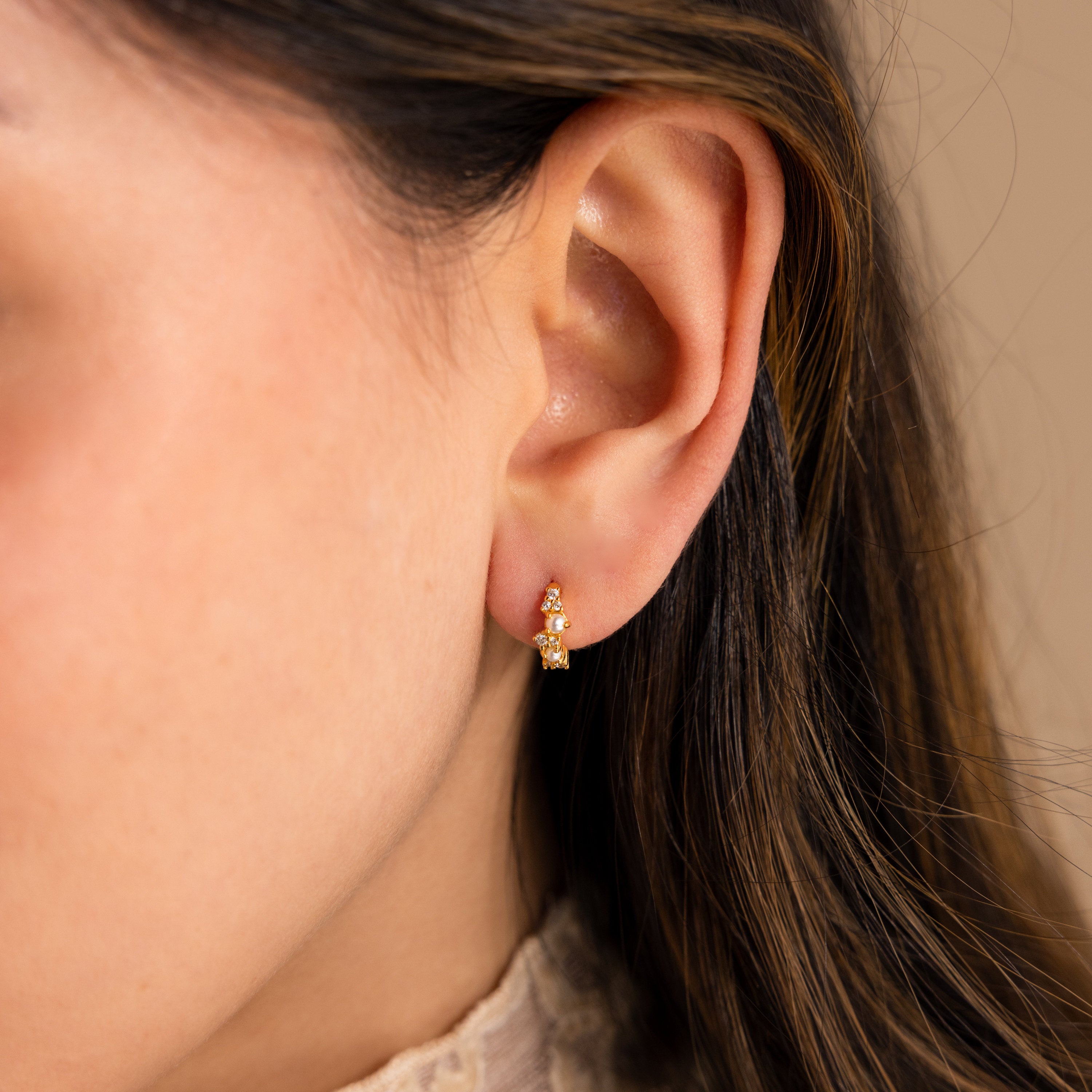 Close-up of a woman's ear wearing Pearl Diamond Cluster Huggies, elegant small gold hoops adorned with pearl and diamond accents.