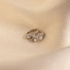 The Pearl Diamond Cluster Huggies, adorned with shimmering pearls and sparkling diamonds, rest on beige textured fabric.