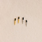 Two pairs of Onyx Dagger Drop Earrings—one gold, one silver—each with baguette-cut onyx stones in a sleek rectangular design, displayed on a beige background.
