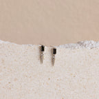 A pair of Onyx Dagger Drop Earrings featuring a sleek dagger charm displayed on a white surface.