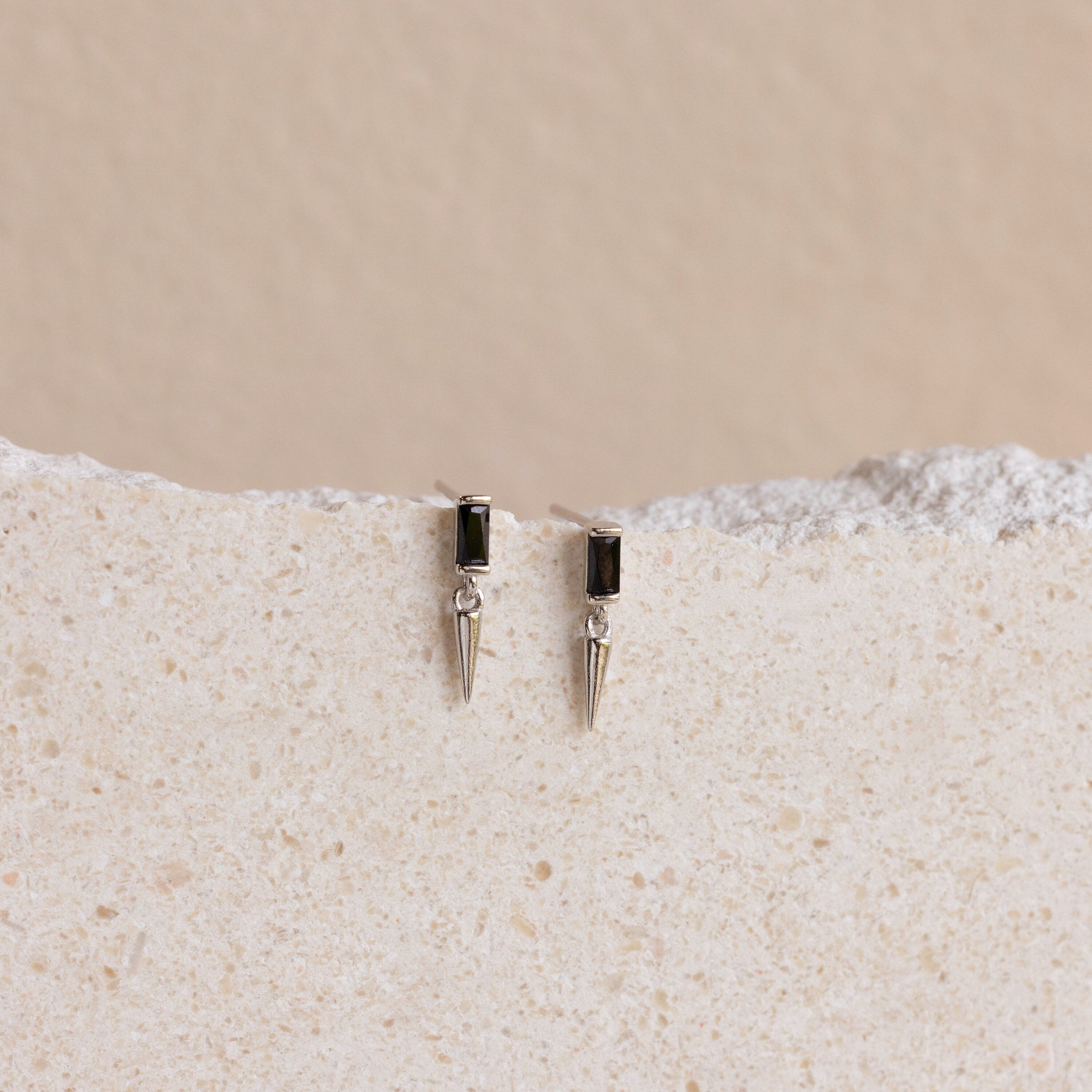 A pair of Onyx Dagger Drop Earrings featuring a sleek dagger charm displayed on a white surface.
