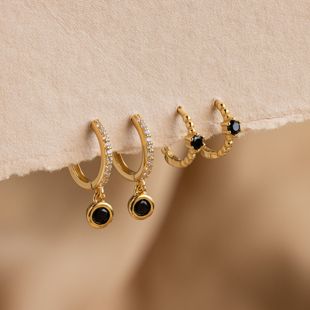 Elegant Pave Onyx Drop Huggies: gold hoops adorned with black onyx gems and sparkling clear stones, plus a small pair featuring bold black stones.