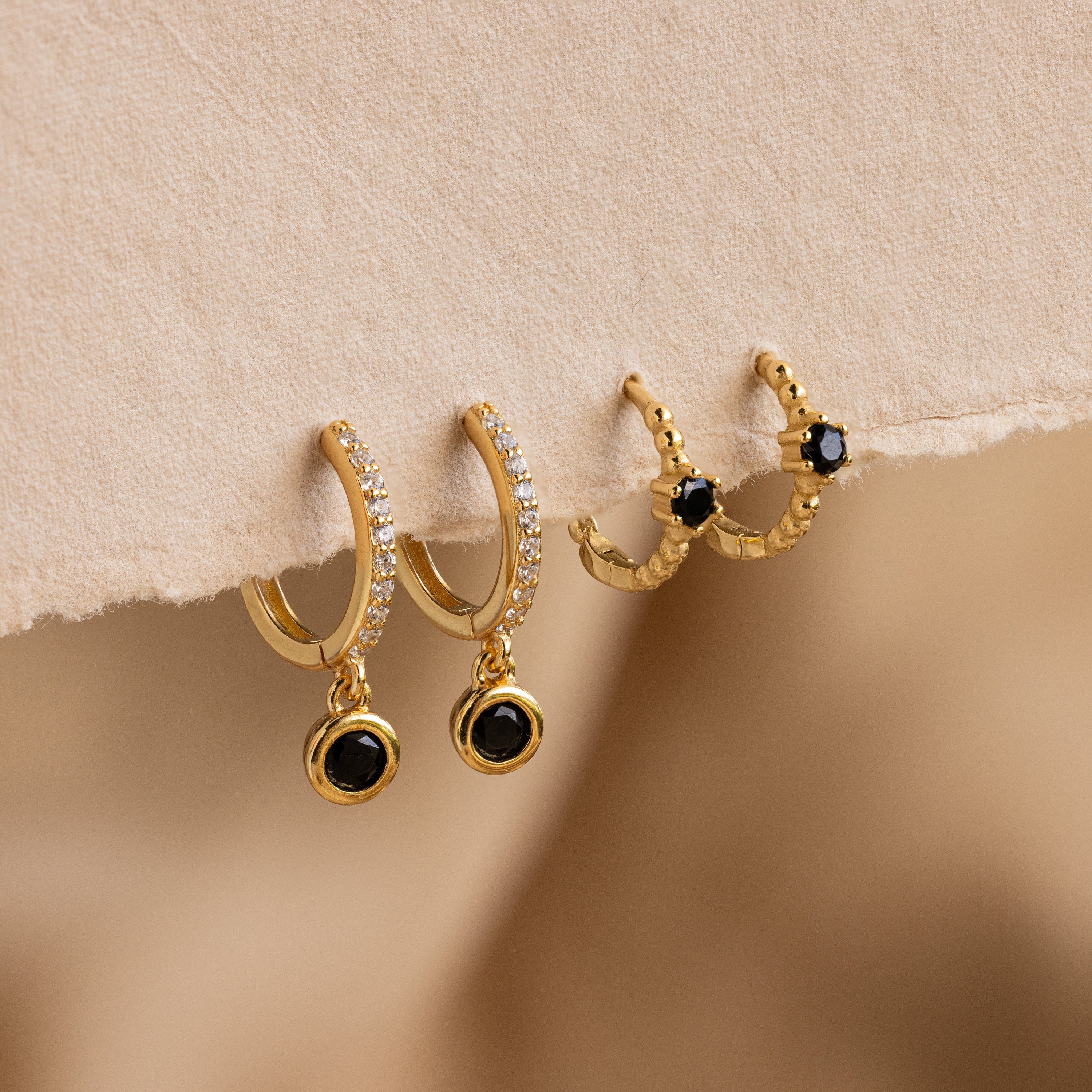 Elegant Pave Onyx Drop Huggies: gold hoops adorned with black onyx gems and sparkling clear stones, plus a small pair featuring bold black stones.