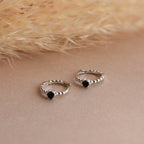 Onyx Beaded Huggies with black stones are displayed on a neutral surface beside dried grass, lending an elegant touch to any look.