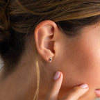 Close-up of a person’s ear adorned with Tiny Onyx Pearl Bar Studs; a hand gently touches the cheek, highlighting the chic minimalist style of these elegant earrings.