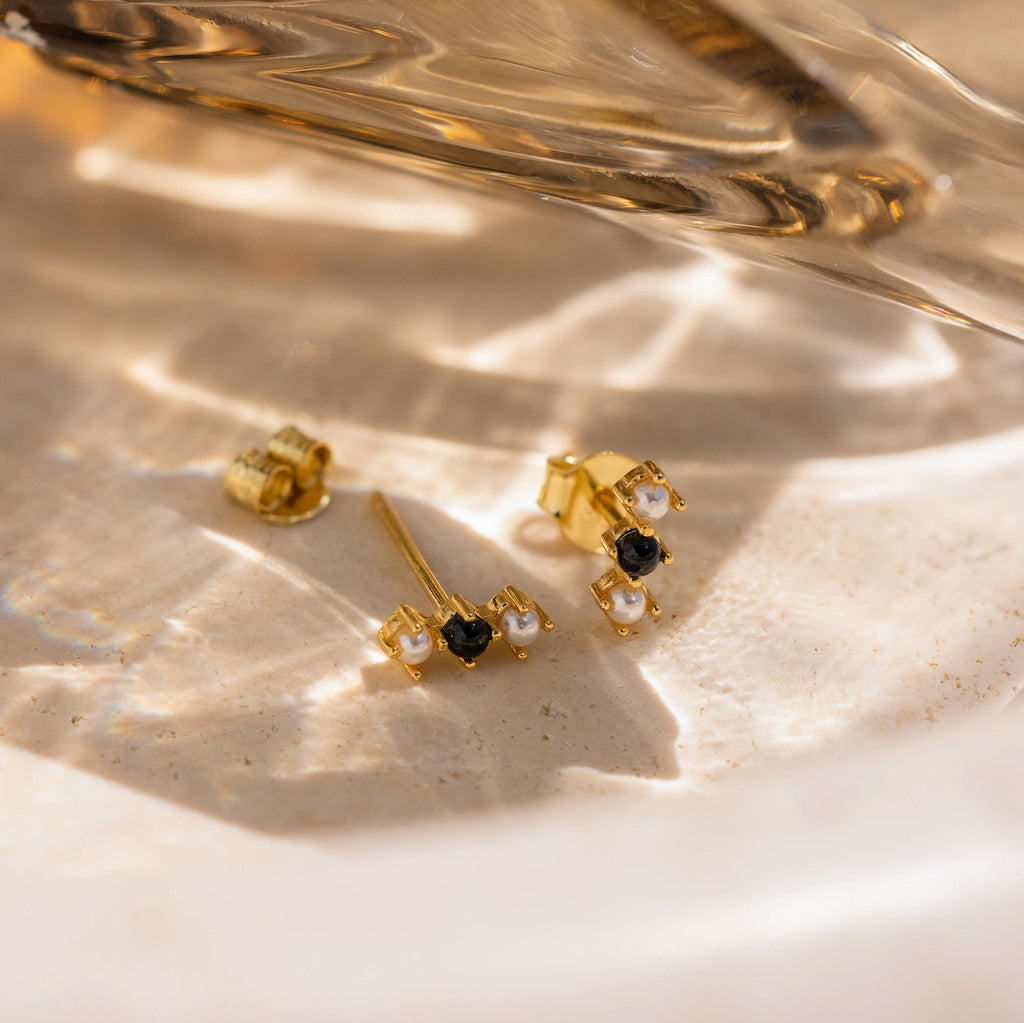 A chic pair of Tiny Onyx Pearl Bar Studs featuring gold bars with black and white stones.