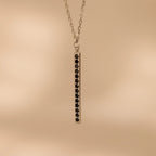 The Onyx Bar Pendant Necklace features a sleek silver bar design with a vertical row of black onyx gemstones.