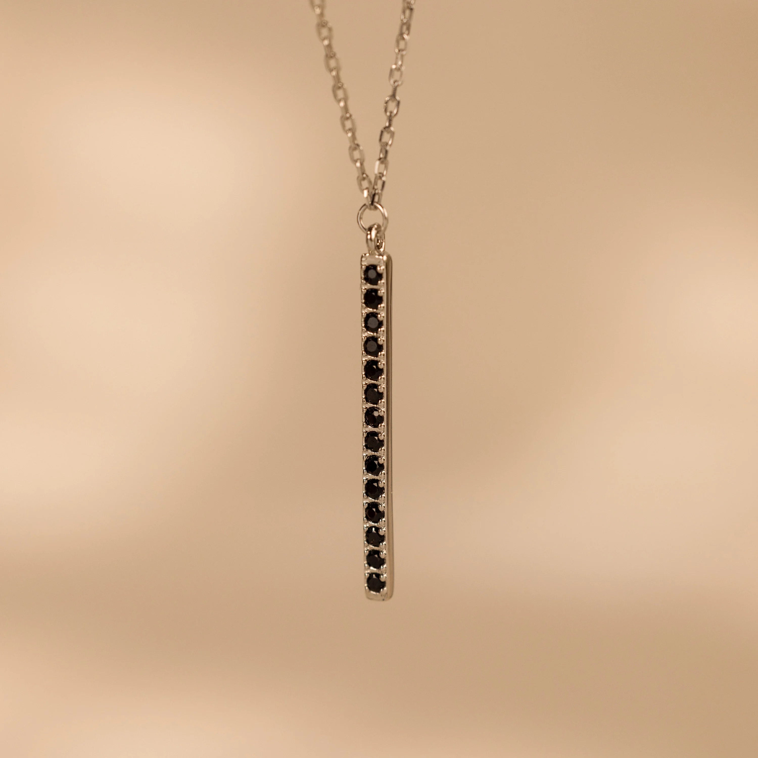The Onyx Bar Pendant Necklace features a sleek silver bar design with a vertical row of black onyx gemstones.