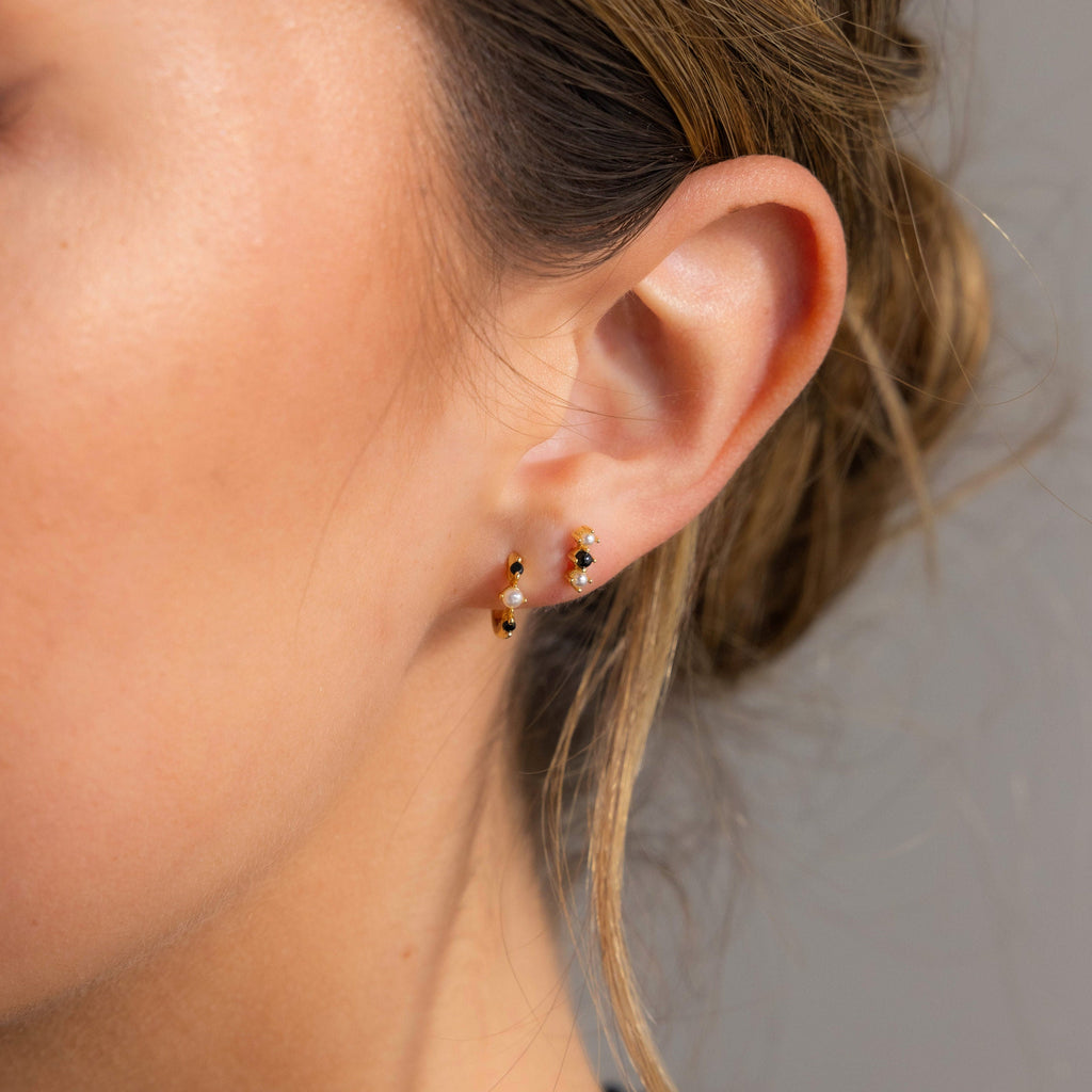 A close-up of a woman’s ear adorned with chic Tiny Onyx Pearl Bar Studs.