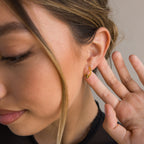 A woman with light brown hair displays the Onyx Pave Beaded Hoops, holding her hand near her ear to highlight the delicate gold earrings.