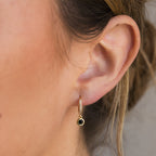 Close-up of a woman's ear adorned with Pave Onyx Drop Huggies, featuring elegant pavé hoops and a striking black onyx gemstone drop for a sophisticated touch.