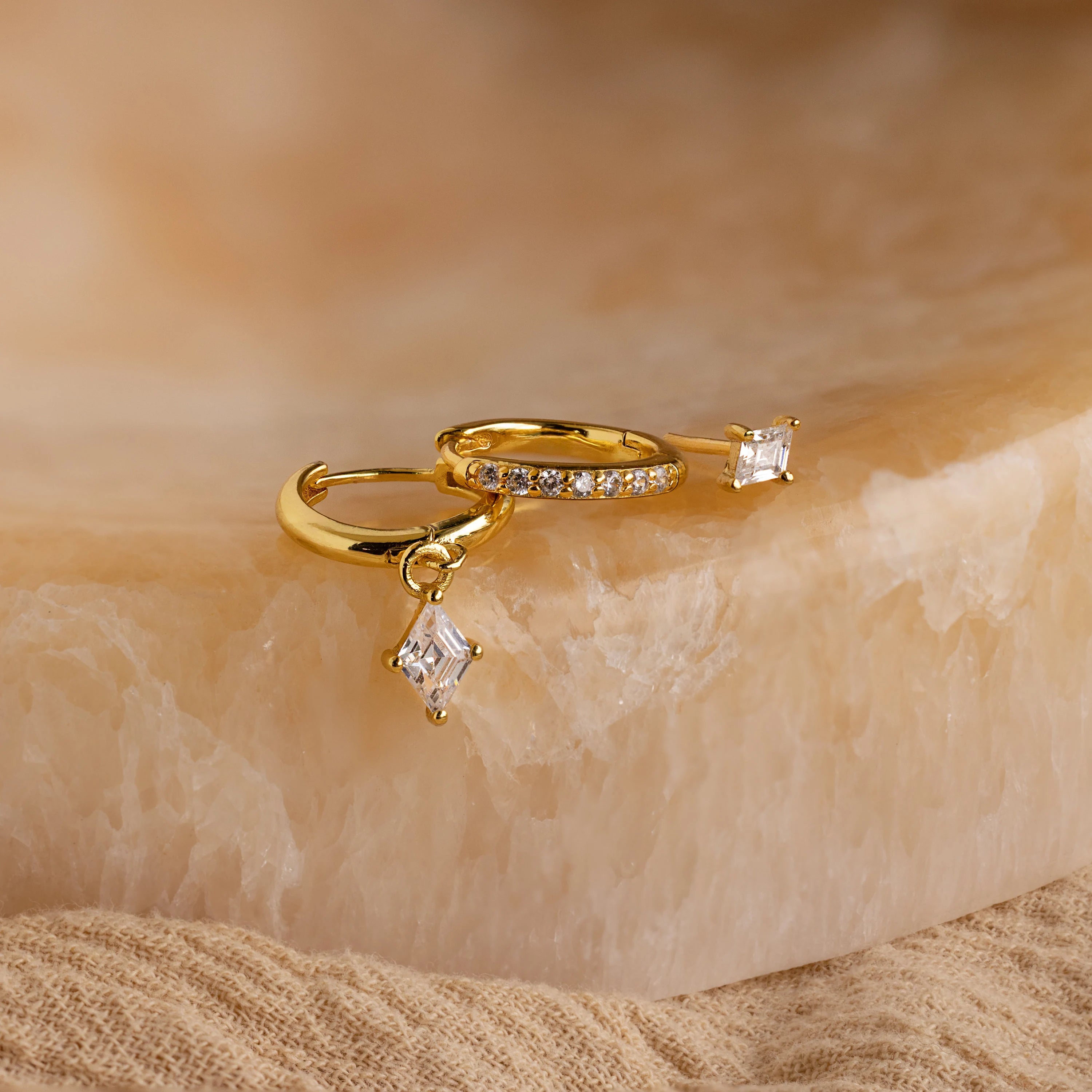 The Diamond Pave Earrings Set features gold hoops with square diamond pendants and embedded clear stones, displayed on beige marble—perfect for adding sparkle to your bridal jewelry collection.
