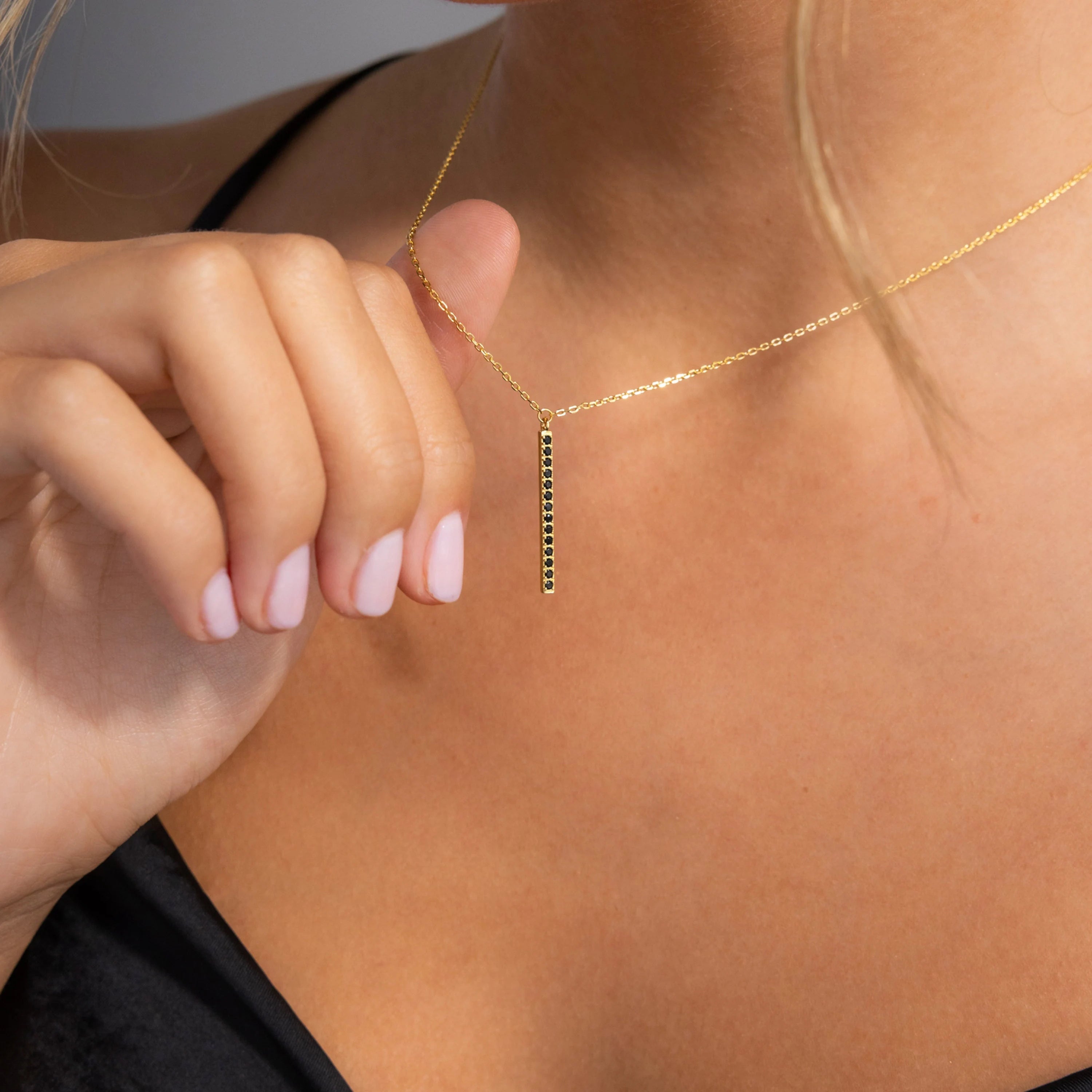 A woman in a black top holds the Onyx Bar Pendant Necklace with its modern bar design near her chest.