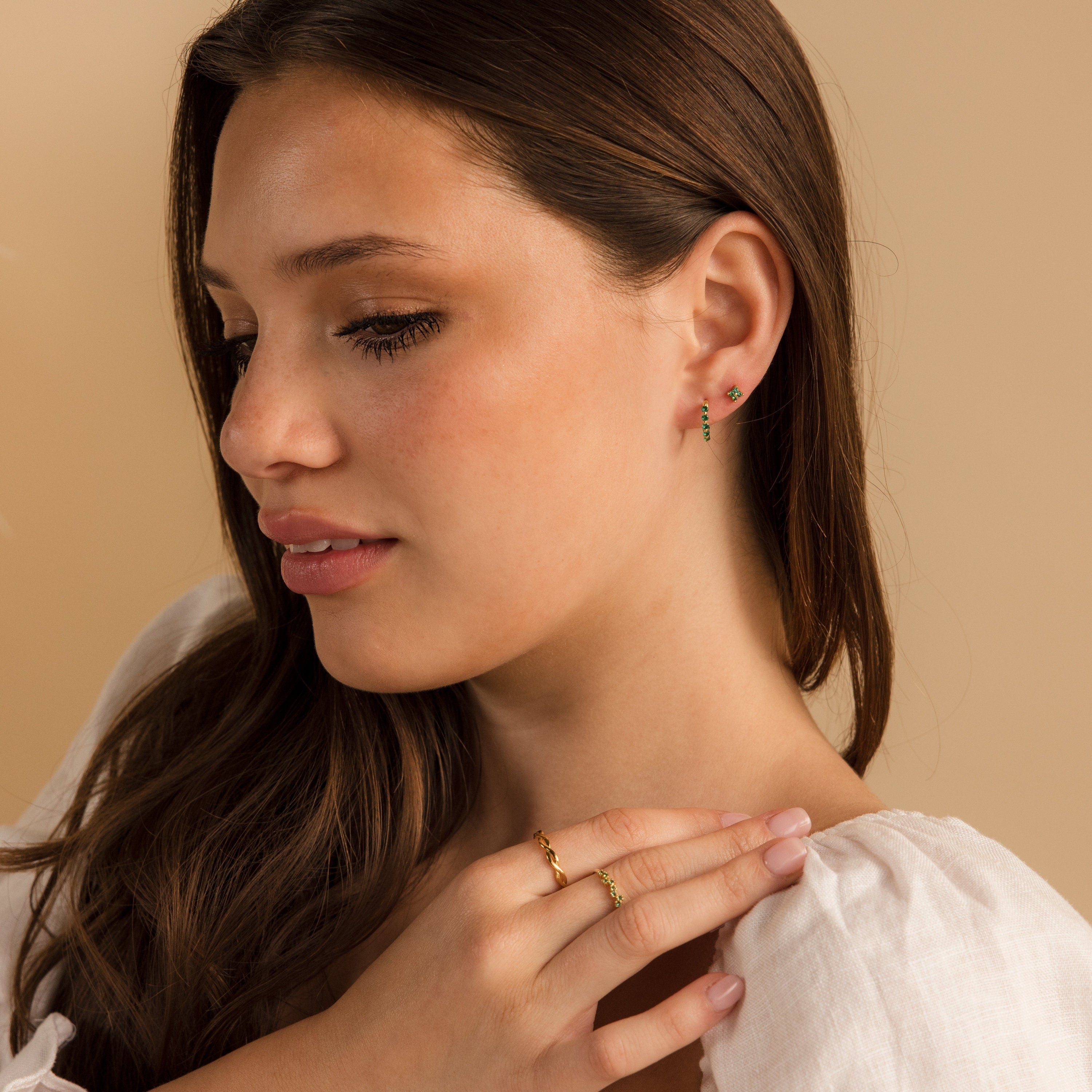 A woman elegantly showcases the Emerald Ivy Flower Studs, nature-inspired jewelry that adds a graceful touch as she rests her hand on her shoulder.