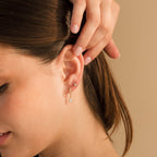 A woman with her brown hair pulled back touches her ear, wearing Diamond Ivy Flower Studs paired with a dangling teardrop earring—a versatile accessory for any occasion.