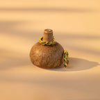 Emerald Marquise Inlay Huggies, elegant birthstone earrings with green gemstones, are displayed alongside gold rings and dainty jewelry on a small brown ceramic vase.