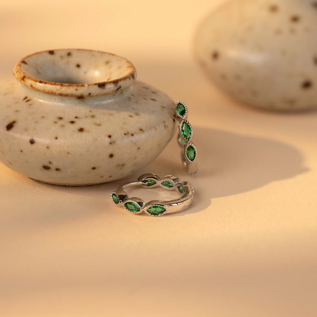 Emerald Marquise Inlay Huggies, ideal for lovers of dainty jewelry, displayed next to a small speckled ceramic pot on a beige surface.