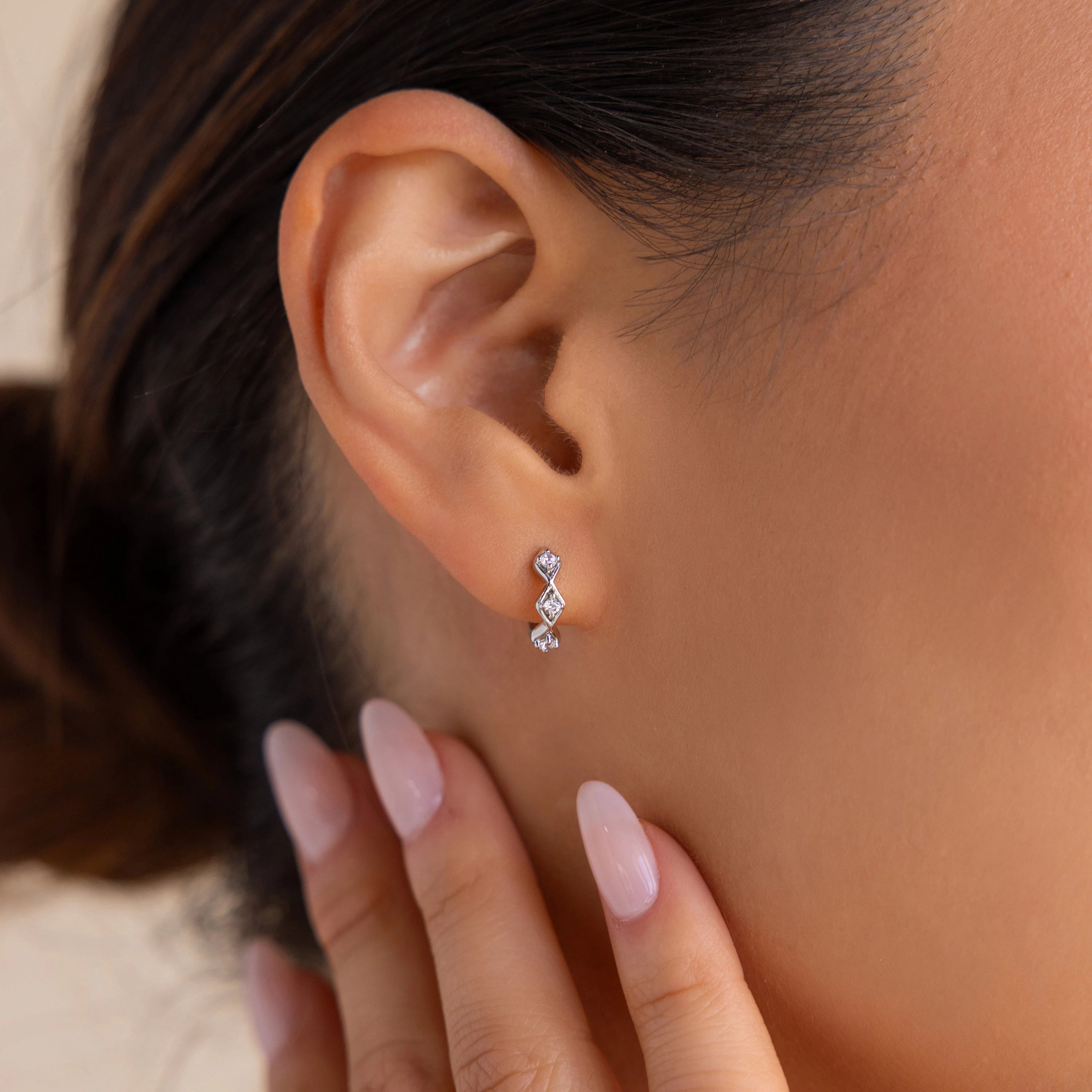 Close-up of a woman's ear wearing Ericka Diamond Tennis Huggies, with manicured fingers gently touching her neck.