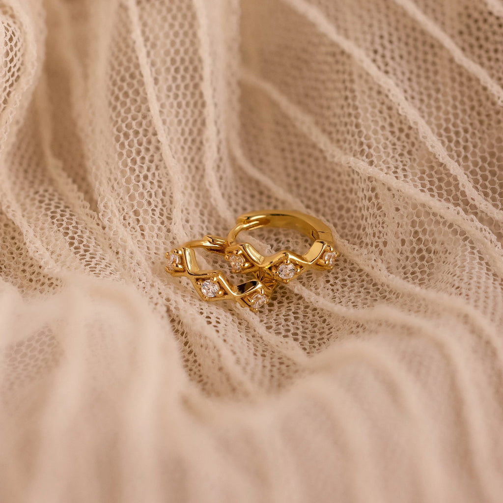 The Ericka Diamond Tennis Huggies are styled with a gold ring on white fabric, creating a timeless and elegant art deco-inspired look.