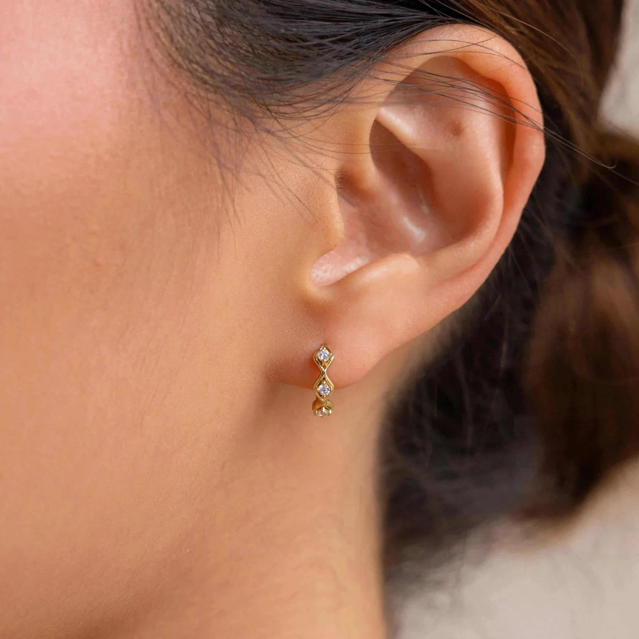 Close-up of a woman's ear wearing the Ericka Diamond Tennis Huggies, small gold earrings with diamonds that add a delicate touch to her look.