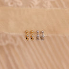 Two pairs of Ericka Diamond Tennis Huggies—one in gold, one in silver—sparkle on a beige fabric background, reflecting the timeless elegance of art deco-inspired earrings.
