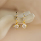 Princess Diamond Drop Studs featuring square princess-cut gemstone pendants and three small round gems, displayed on a cream background.