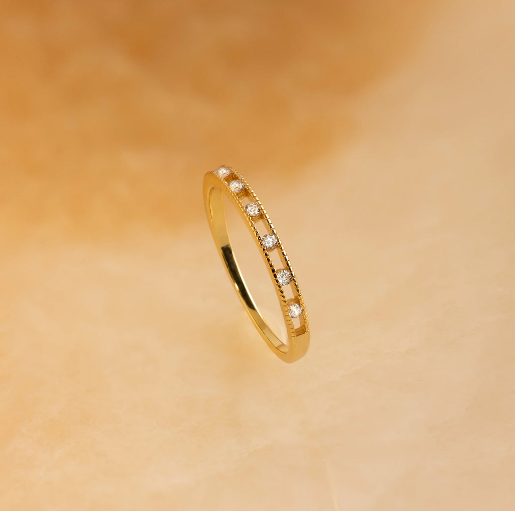 The Diamond Station Ring features small white gemstones evenly set around the band and is shown on a soft beige background. Ideal as a promise or engagement ring.