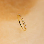 The Diamond Station Ring features small white gemstones evenly set around the band and is shown on a soft beige background. Ideal as a promise or engagement ring.