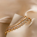 The Pear Diamond Tennis Bracelet, crafted with pear-cut diamonds, is displayed on soft beige satin alongside two other gold and diamond bracelets.