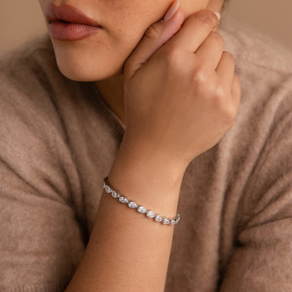 A woman models the Pear Diamond Tennis Bracelet on her wrist, paired with a cozy brown sweater.