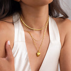 A woman wears the Diamond Ribbed Heart Necklace layered with gold necklaces, paired with a cream sleeveless V-neck top.