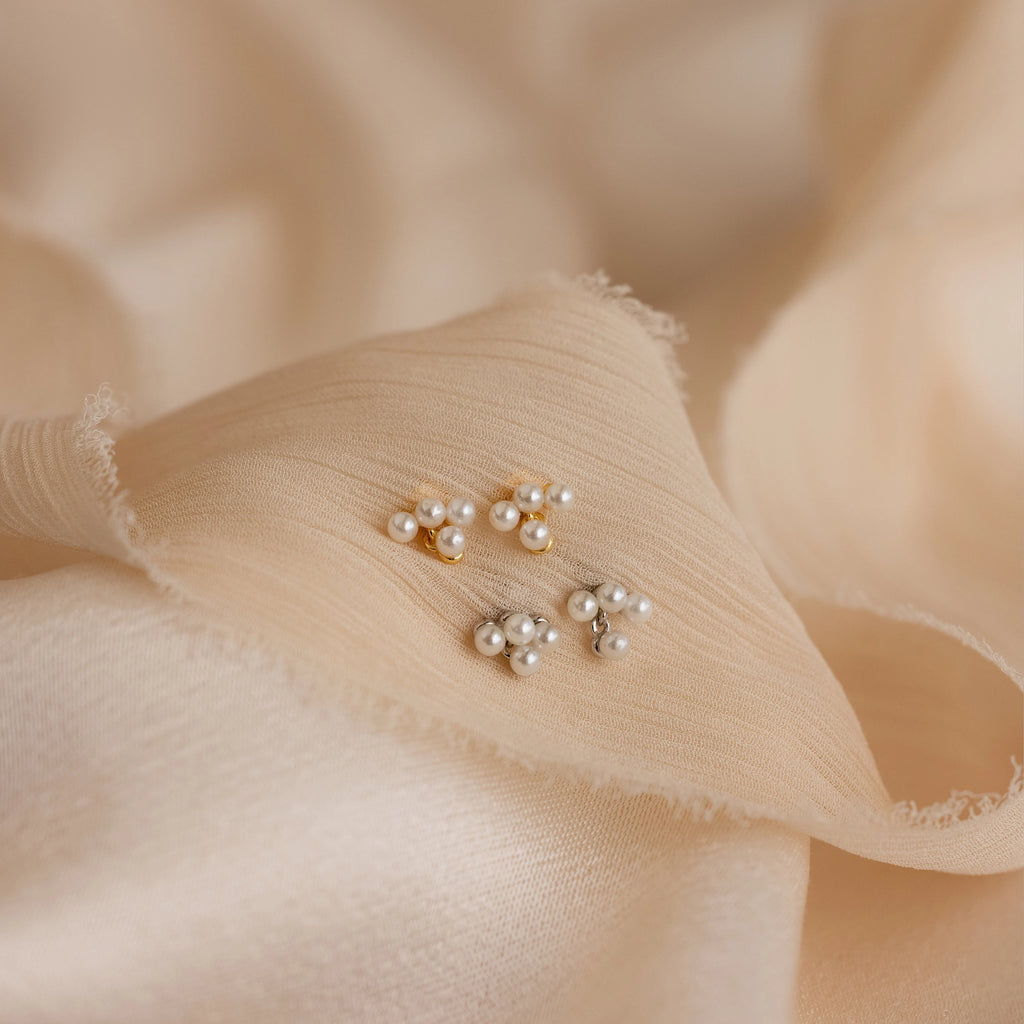 Two pairs of Pearl Cluster Drop Studs rest on soft, textured beige fabric—ideal bridal earrings and an elegant wedding accessory.