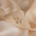 Two pairs of Pearl Cluster Drop Studs rest on soft, textured beige fabric—ideal bridal earrings and an elegant wedding accessory.