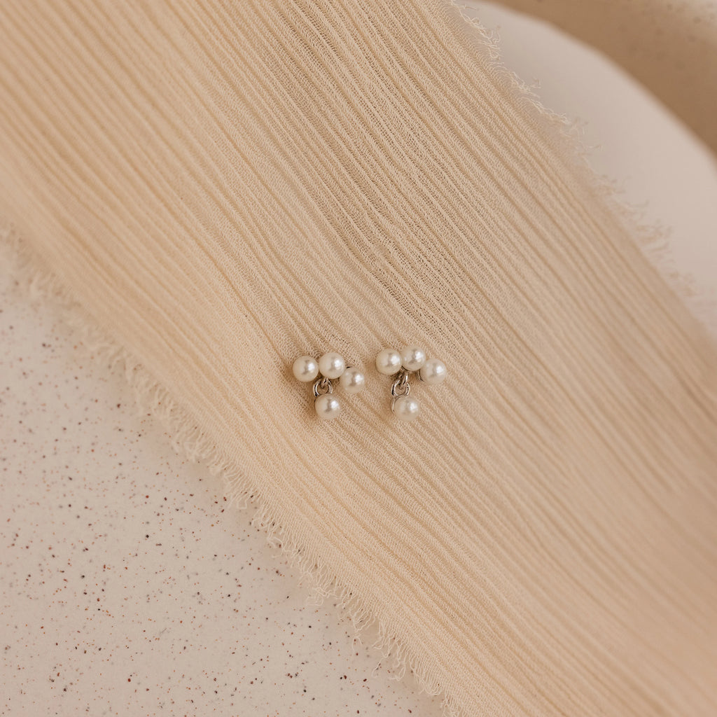 The Pearl Cluster Drop Studs, a timeless bridal earring and elegant wedding accessory, rest on textured, beige fabric.