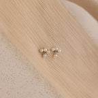 The Pearl Cluster Drop Studs, a timeless bridal earring and elegant wedding accessory, rest on textured, beige fabric.