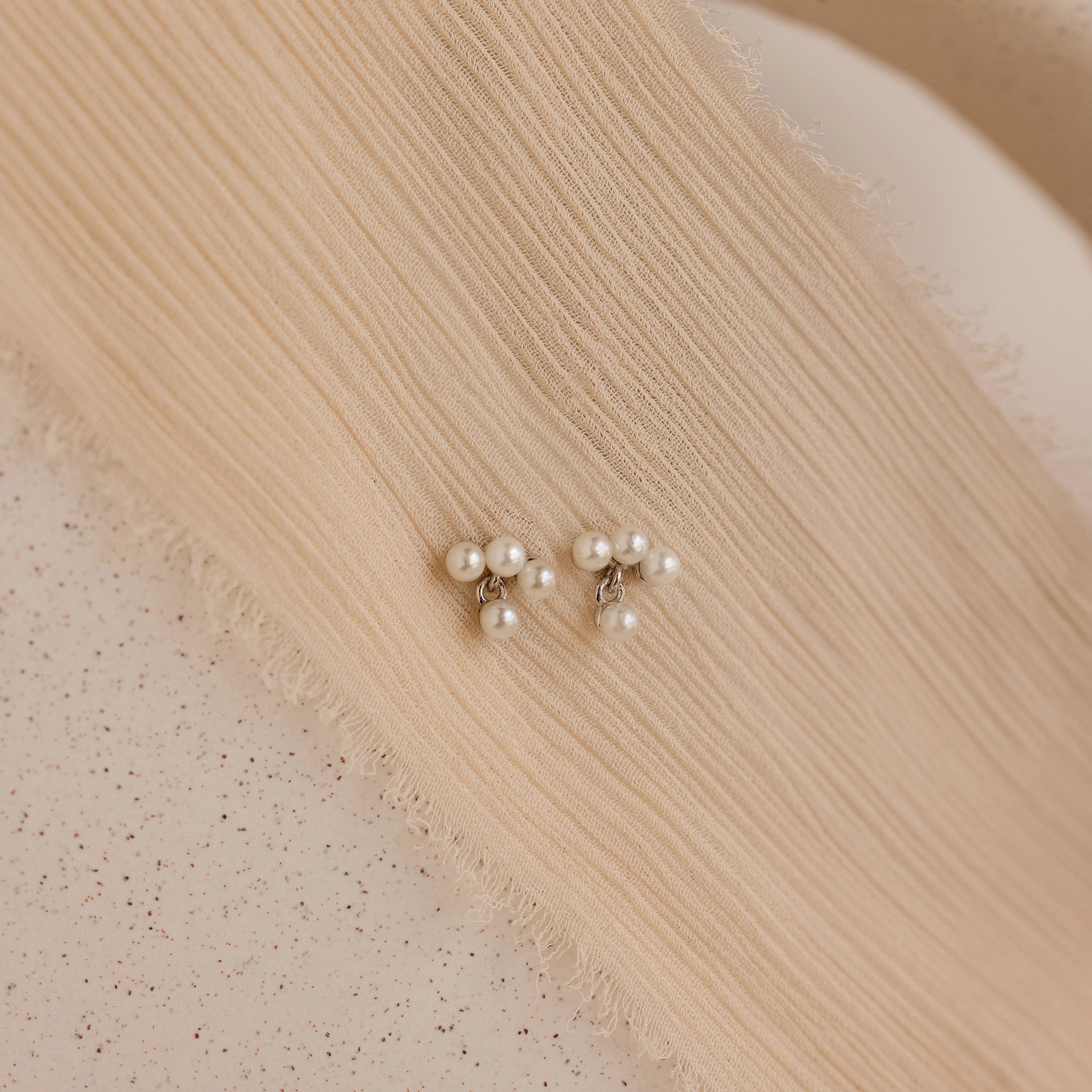 The Pearl Cluster Drop Studs, a timeless bridal earring and elegant wedding accessory, rest on textured, beige fabric.