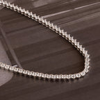 The 3 Prong Tennis Necklace, featuring sparkling heart-shaped diamonds, rests on a glossy brown surface.