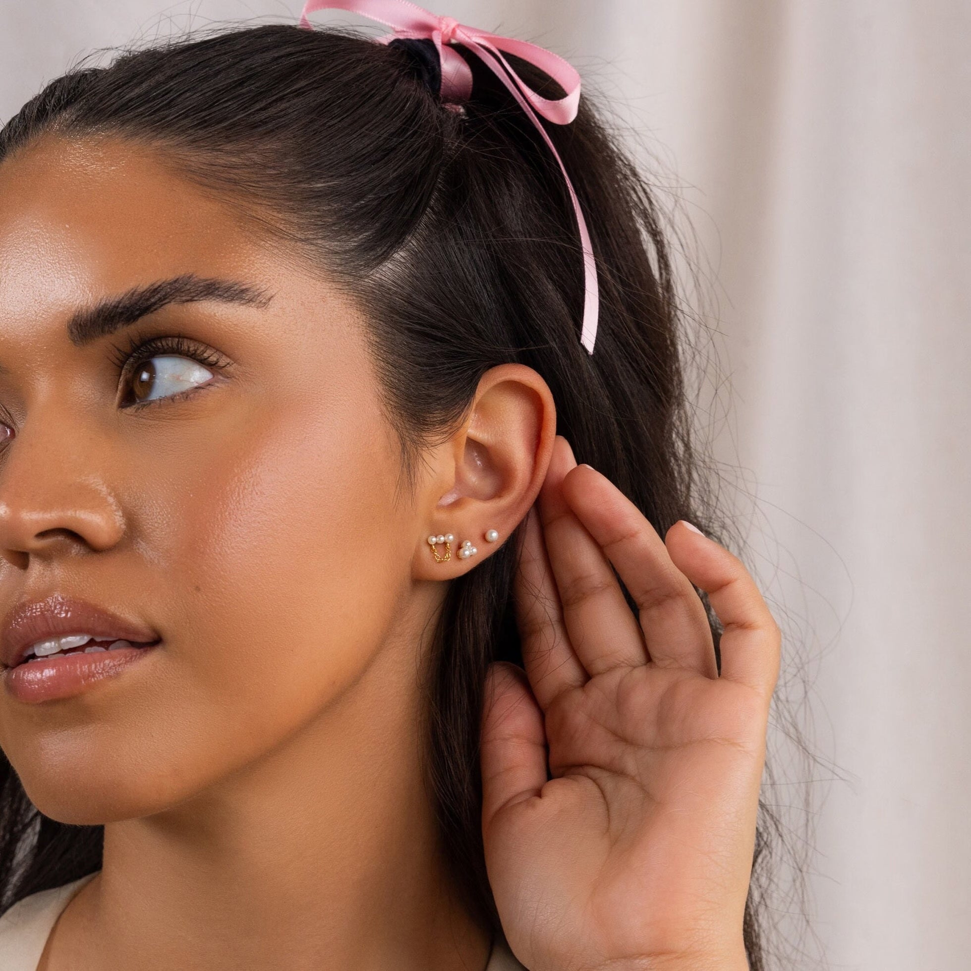A woman with a pink hair ribbon holds her hand to her ear, drawing attention to the elegant Pearl Bar Chain Studs.