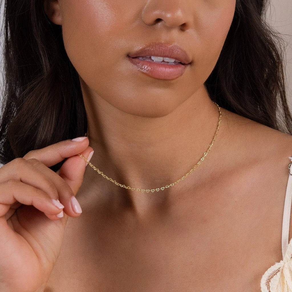 A woman gently holds the Heart Link Chain Necklace near her collarbone, showcasing its delicate, romantic design.