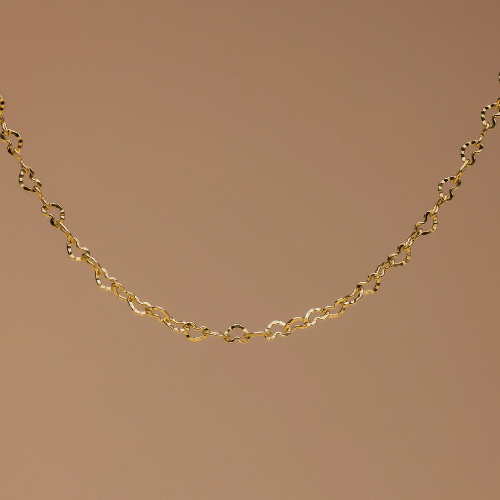 The Heart Link Chain Bracelet features small, repeating heart-shaped links for a romantic look, elegantly displayed against a plain brown background.