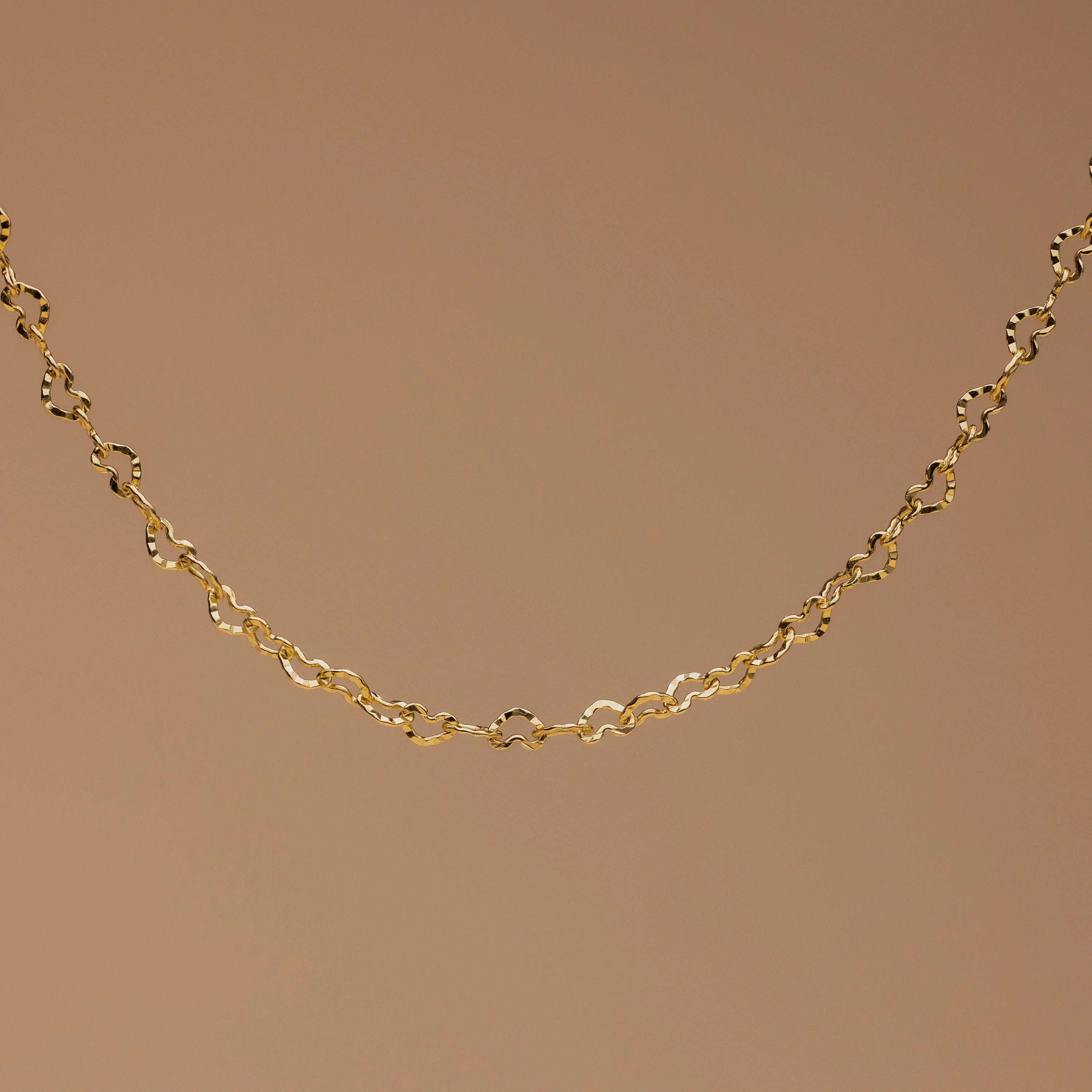 The Heart Link Chain Bracelet features small, repeating heart-shaped links for a romantic look, elegantly displayed against a plain brown background.