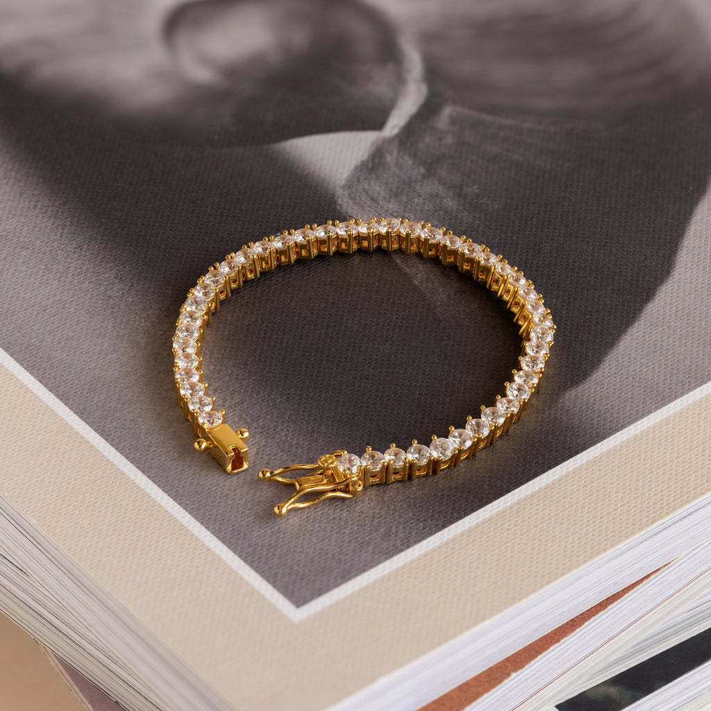 The 3 Prong Tennis Bracelet with clear gemstones rests atop a stack of books, making an elegant statement piece.