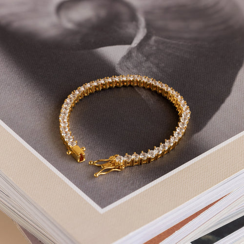 The 3 Prong Tennis Bracelet with clear gemstones rests atop a stack of books, making an elegant statement piece.