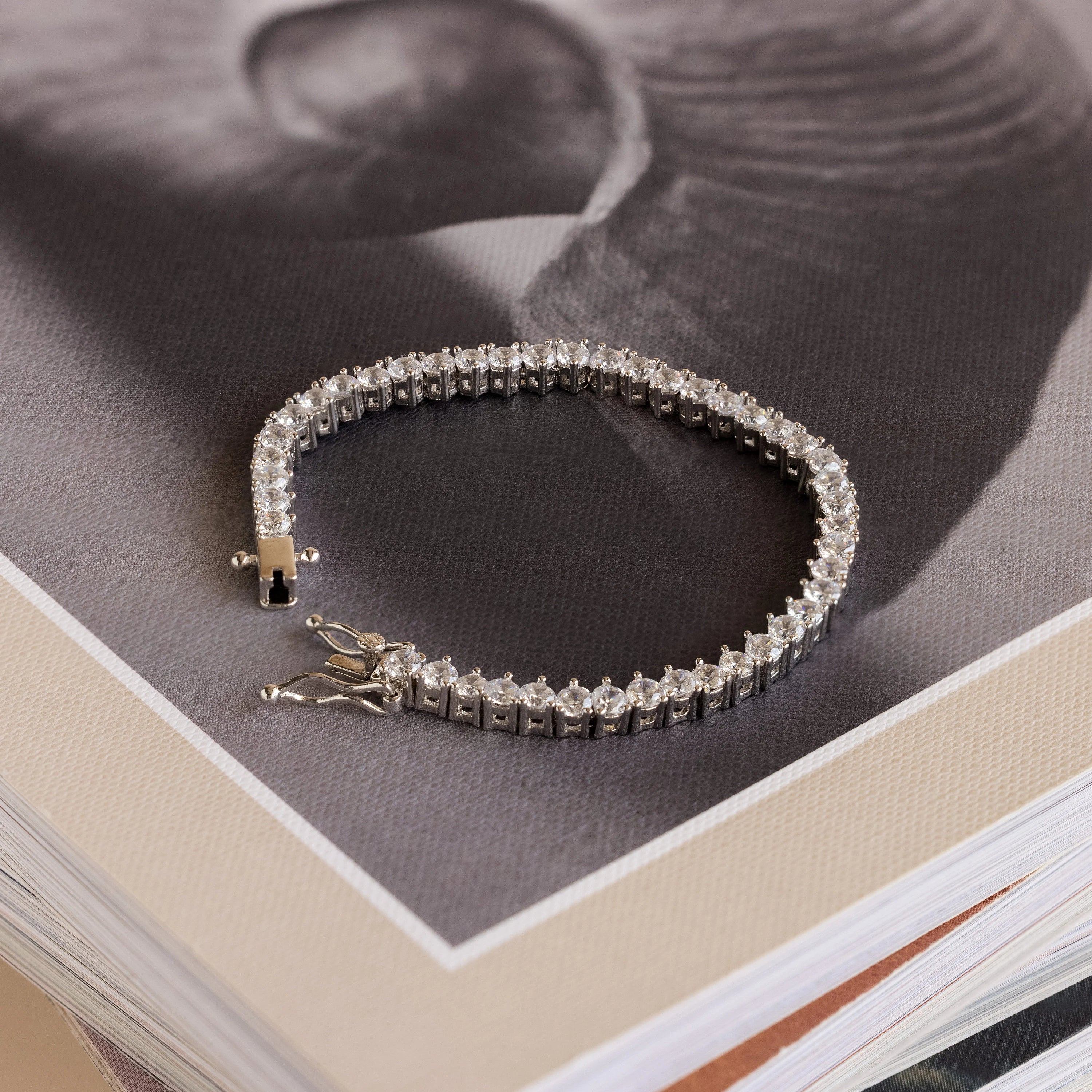 The 3 Prong Tennis Bracelet, a stunning statement piece, is elegantly displayed atop a book featuring a black and white photograph on its cover.