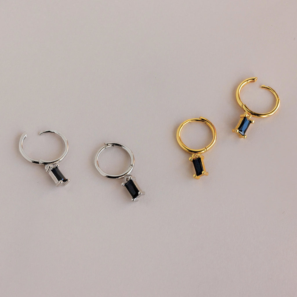 Two pairs of Onyx Baguette Drop Huggies—one in silver, one in gold—each featuring a rectangular black onyx stone. Perfect for adding a stylish touch to any occasion.