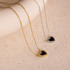 The Pave Onyx Heart Necklace in Sterling Silver features a heart-shaped pendant with delicate pave CZ diamonds, displayed on a textured surface for an elegant, sparkling look.